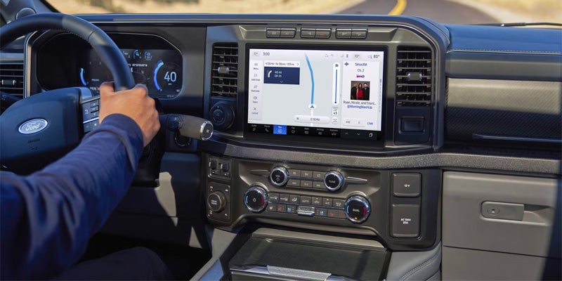 Truck interior with touchscreen navigation, driver holding steering wheel.